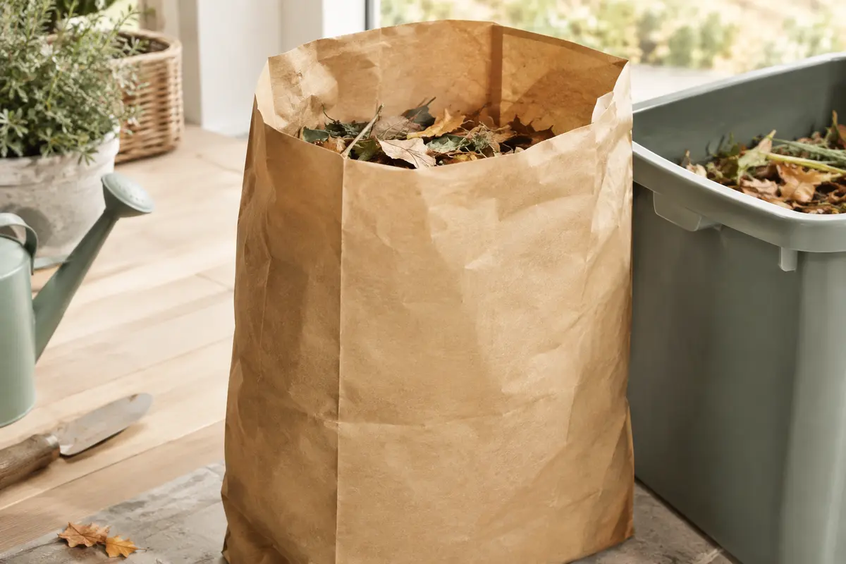 Sac brun en papier kraft à fond renforcé, ouvert près d’un bac de déchets de jardin.