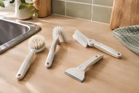 Lot de quatre brosses blanches de nettoyage posé près d’un évier et d’un carreau mat.