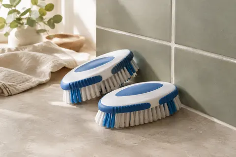 Deux brosses ovales blanches et bleues à poils fermes posées près d’un carrelage et de ses joints.