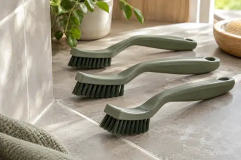 Trois brosses à joints Nori à tête incurvée près d’un carrelage, avec leurs poils fermes visibles.