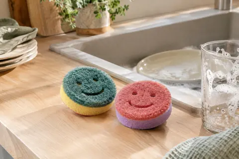 Deux éponges Scrub Mommy multicolores à double face posées près d’un évier de cuisine