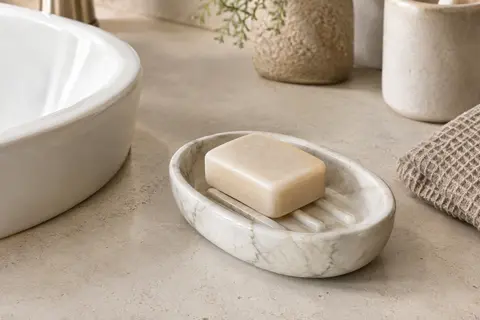 Porte-savon ovale en céramique blanche à motif marbré, posé près d’un lavabo avec un savon solide.