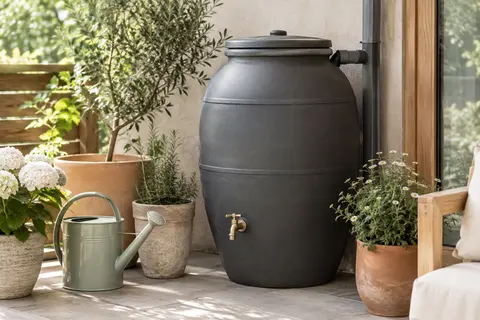 Récupérateur d’eau de pluie anthracite en forme d’amphore, avec panier filtrant et robinet sur une terrasse.